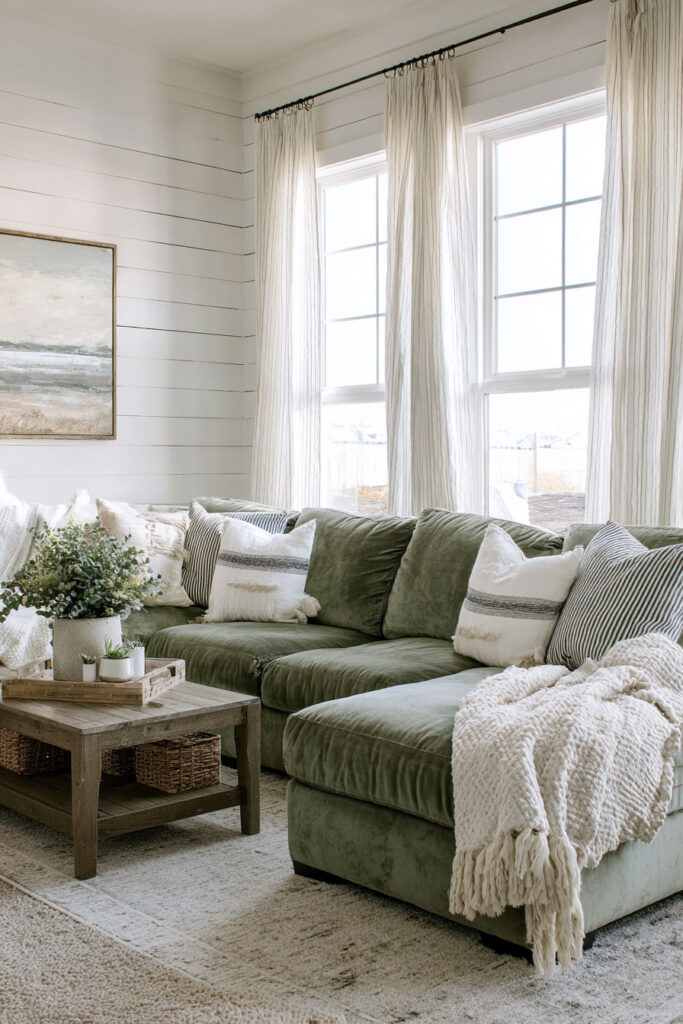 Farmhouse living room with sage green sectional sofa, white shiplap walls, rustic wood coffee table, and layered cozy pillows.
