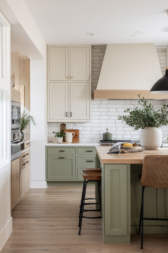 Two-tone sage green kitchen with shaker cabinets, butcher block island, woven barstools, and white brick backsplash.
