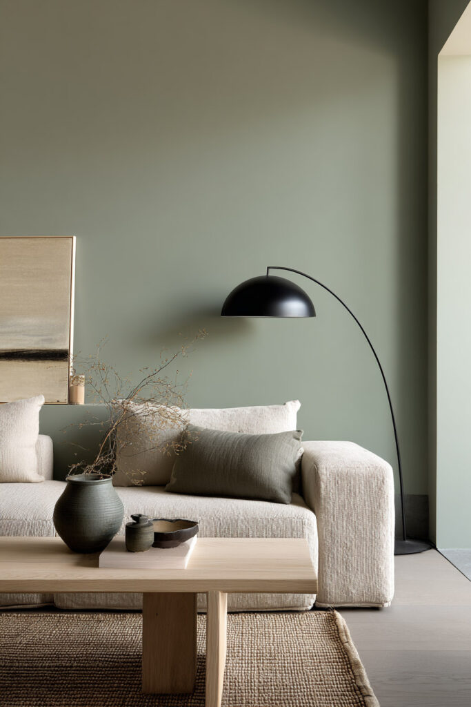 Minimalist sage green living room with textured neutral sofa, black arc floor lamp, wood coffee table, and ceramic vase accents
