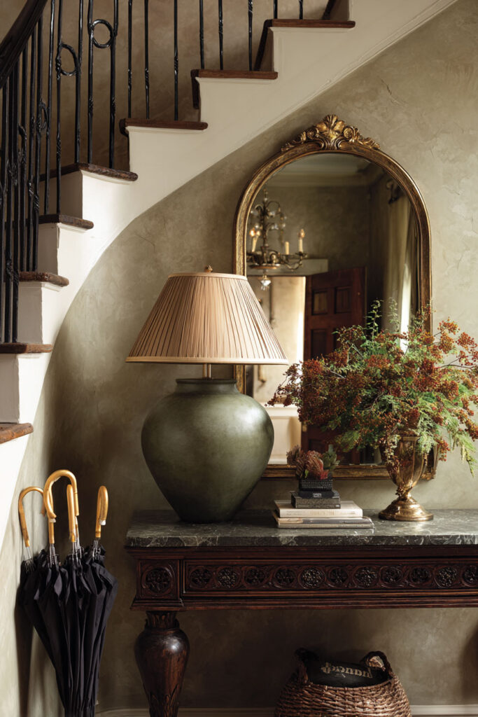 Elegant sage green entryway with ornate console table, antique gold mirror, marble tabletop, classic lamp, and greenery arrangement.