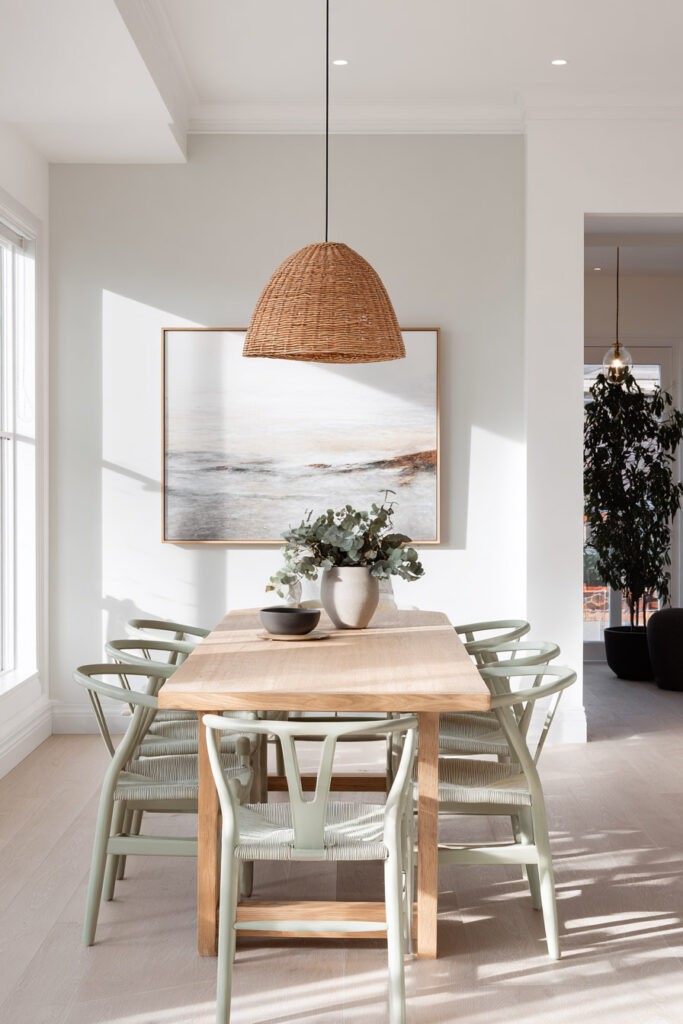 Dining room with sage green wishbone chairs, light wood table, woven pendant light, and minimalist wall art.
