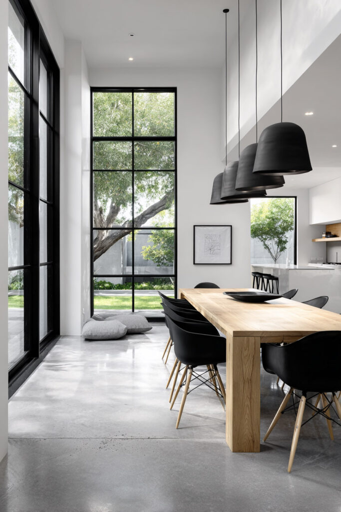 Modern black and white dining room with a light wood table, black chairs, pendant lights, and tall grid-style windows bringing in natural light.