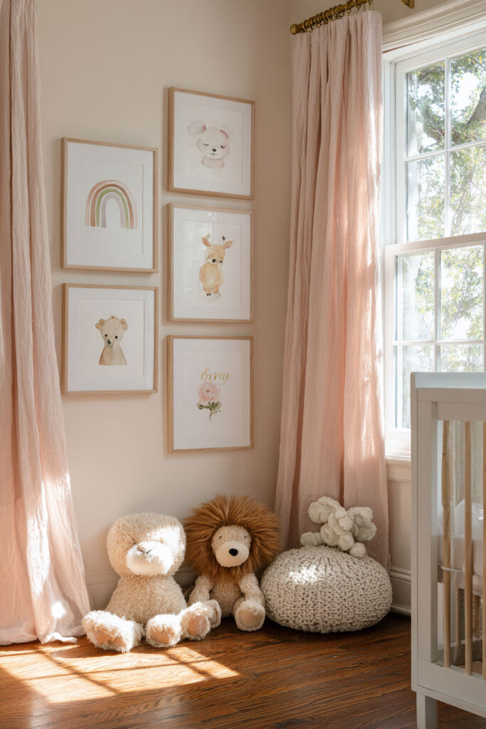 Cozy nursery with blush curtains, watercolor animal art gallery wall, plush toys, and natural wood accents in soft sunlight.