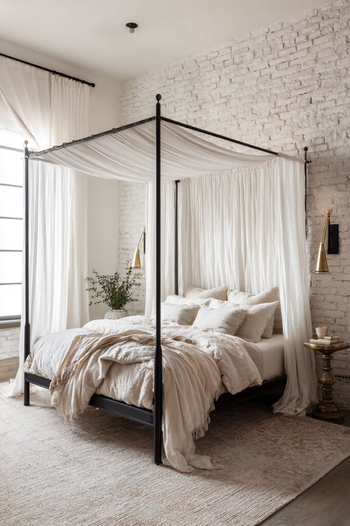 Romantic black and white bedroom with a canopy bed, sheer white curtains, white brick wall, brass sconces, and soft layered bedding.