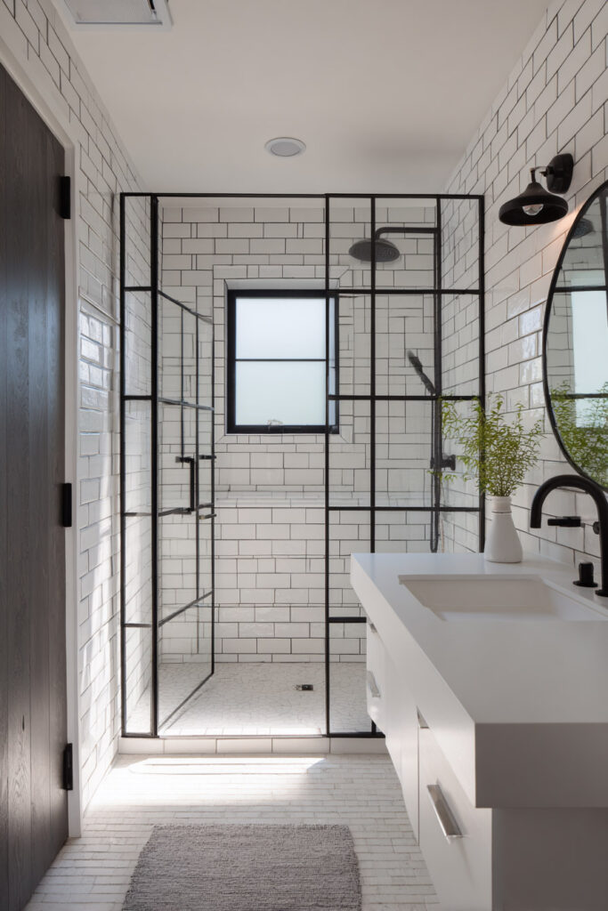Modern black and white bathroom featuring a glass shower with black grid framing, white subway tile walls, matte black fixtures, and a sleek white vanity.