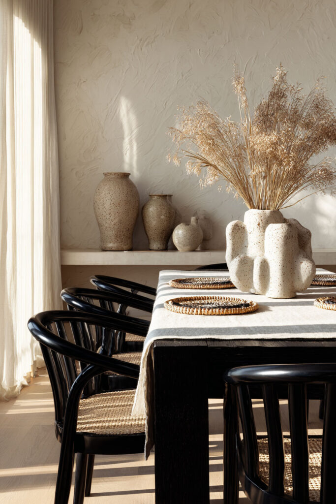 Elegant black and white dining room with black chairs, woven placemats, textured ceramic vases, and dried grass centerpiece on a linen table runner.