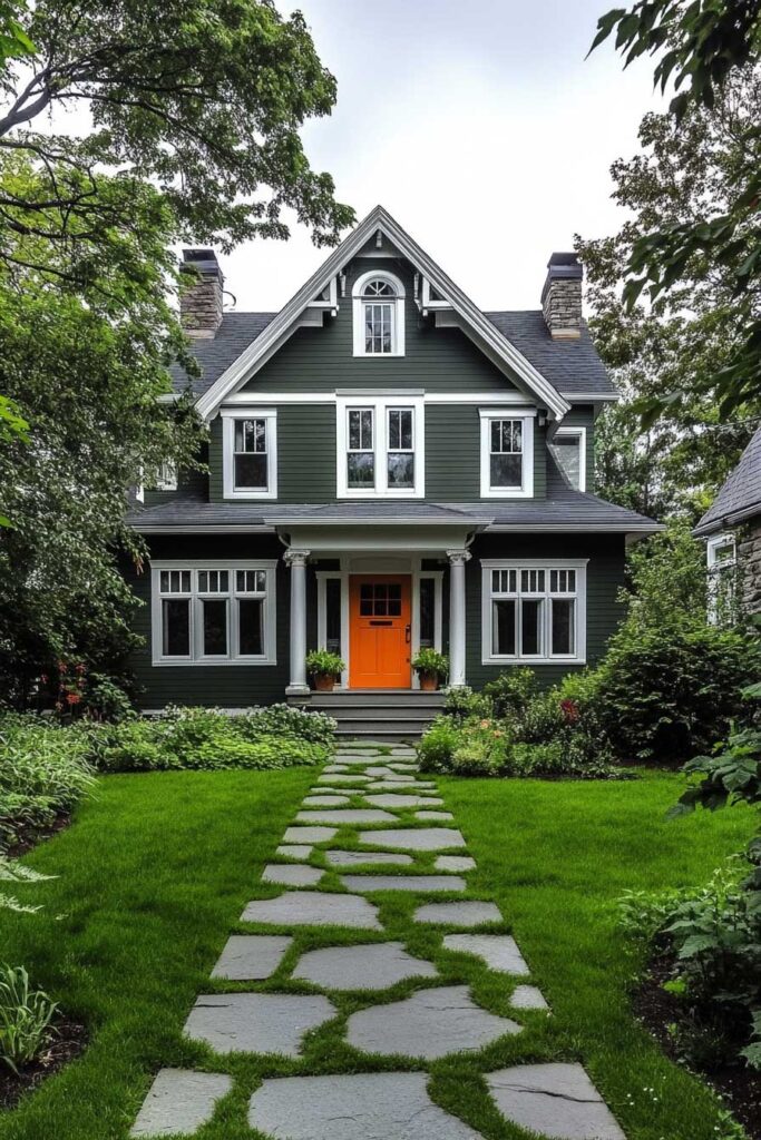 Dark green house with white trim, orange front door, stone walkway, and lush garden landscaping.
