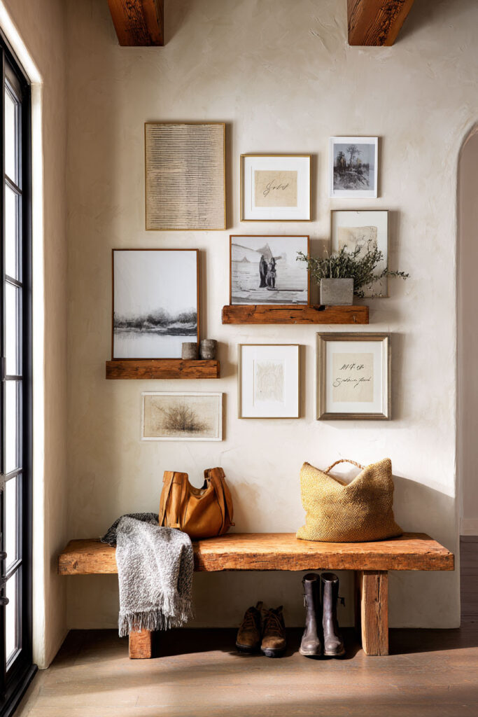Rustic entryway with wood bench, layered framed art on ledges, leather bag, and cozy throw blanket.