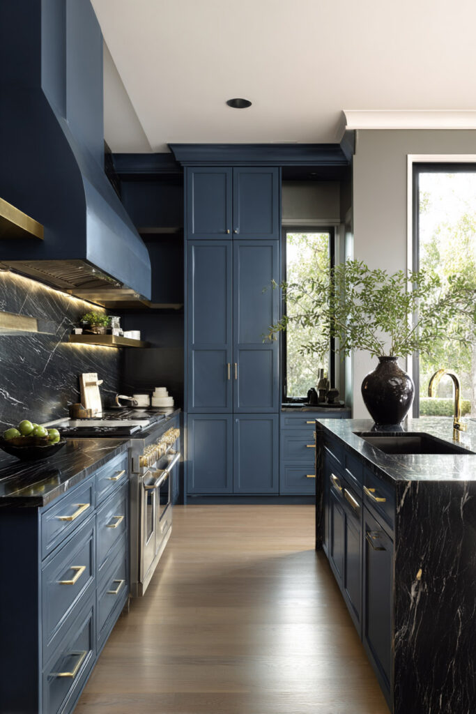 Moody navy kitchen with black marble counters, brass hardware, and natural light creating a modern, sophisticated atmosphere.