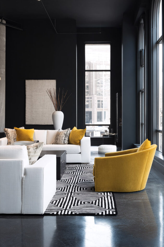 Modern black and white living room with mustard yellow accent chairs, geometric rug, and large industrial-style windows.