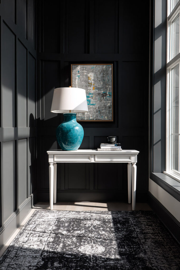 Modern black paneled room with white console table, teal lamp, and sunlight casting shadows in a bold black-and-white color palette.