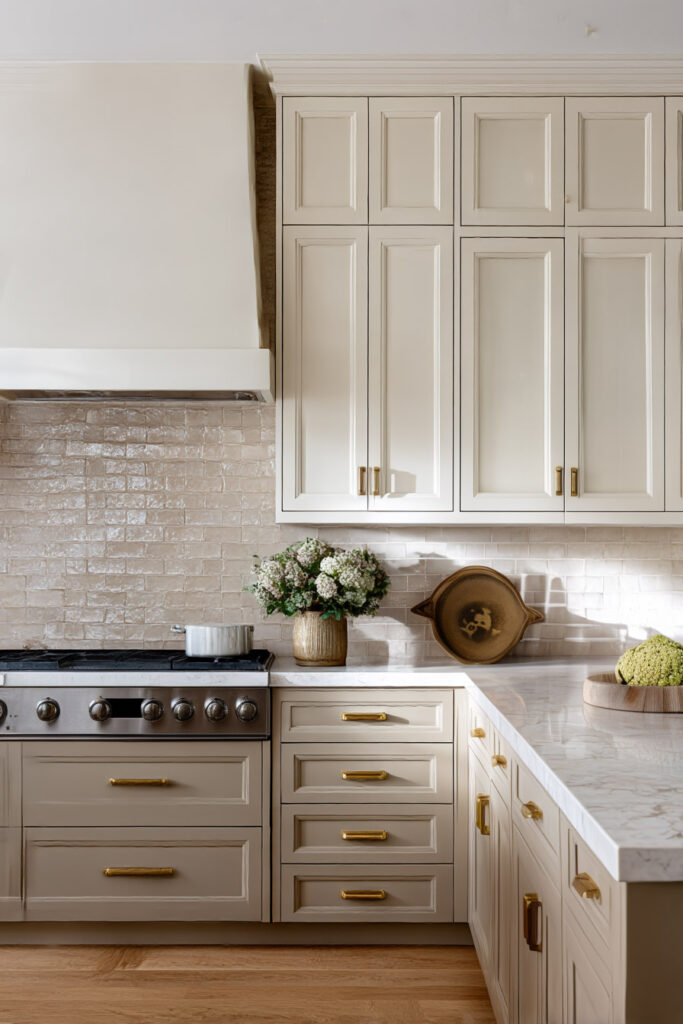 Warm neutral kitchen with cream cabinets, zellige tile backsplash, brass hardware, marble countertops, and stainless range.