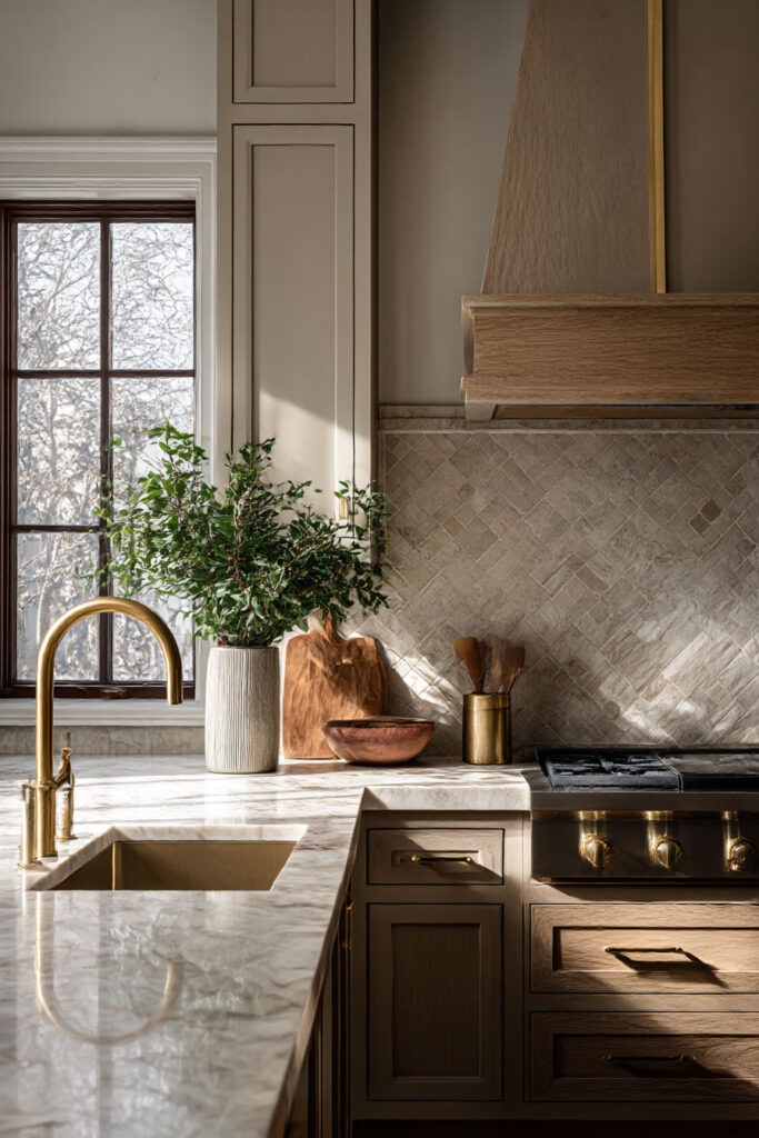 Warm neutral kitchen with oak cabinets, creamy uppers, textured tile backsplash, marble countertops, and brass faucet.