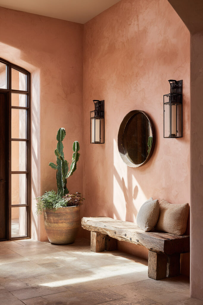 Warm desert entryway with blush plaster walls, rustic wood bench, potted cactus, round mirror, and soft natural sunlight.