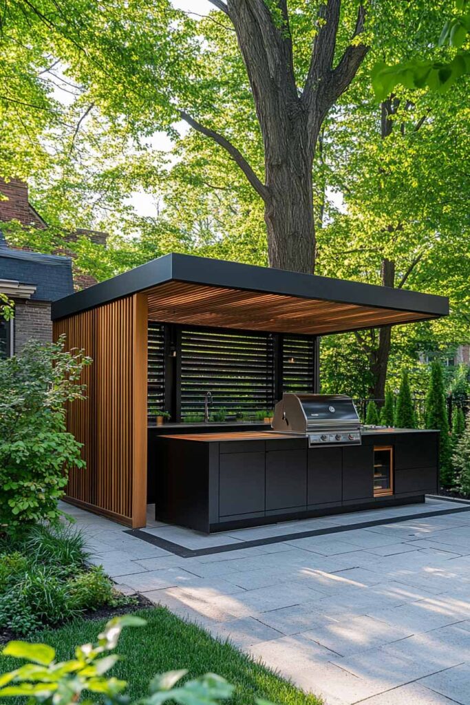 Modern outdoor grill station with black cabinets, built-in grill, wood slat privacy panels, and a flat roof pergola in a landscaped backyard.