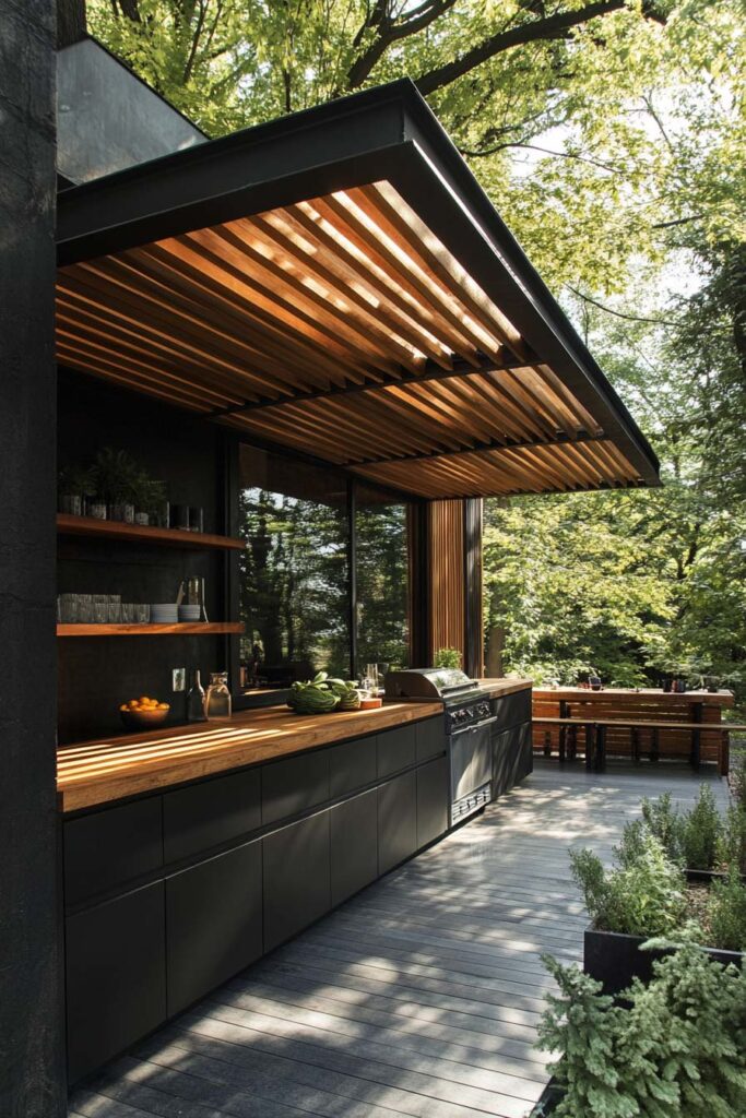 Modern outdoor grill station with black cabinets, wood countertops, slatted pergola roof, and forest-style backyard setting