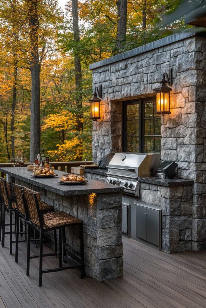 Outdoor grill station with stone walls, built-in stainless steel grill, bar seating, granite countertop, and lantern lighting on a wooded deck.