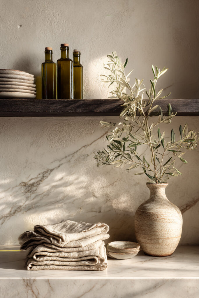Kitchen stone backsplash with open wood shelf, neutral ceramics, olive branches, and natural styling