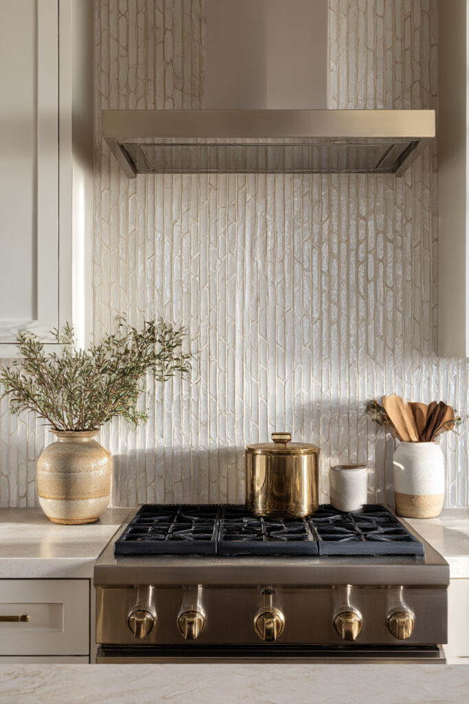 Vertical stone tile kitchen backsplash with brass range, neutral cabinetry, and earthy styling