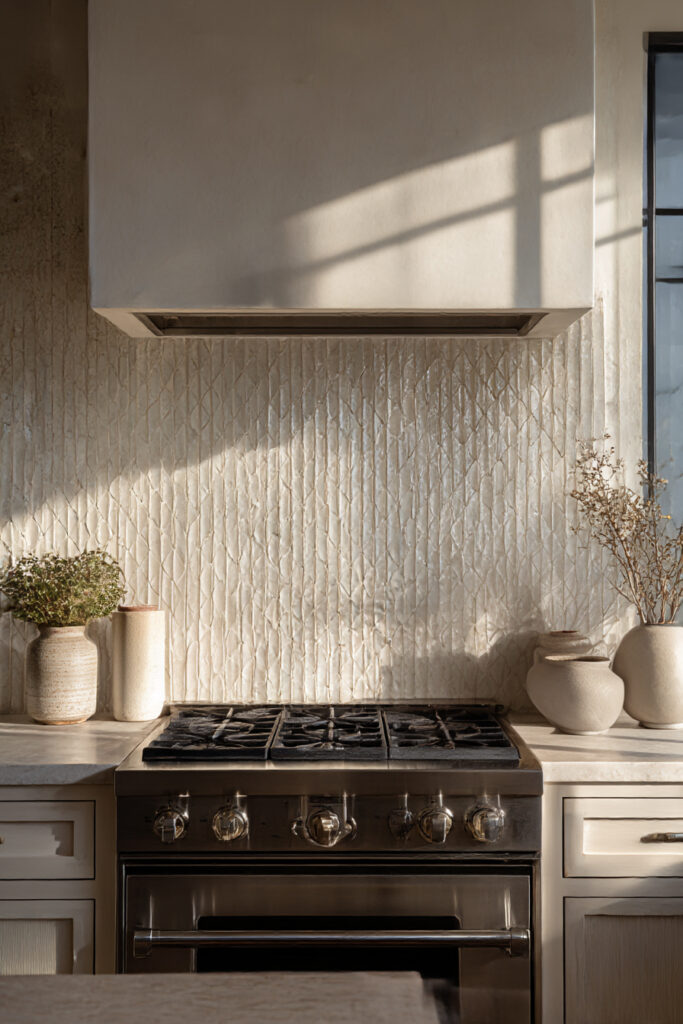 Kitchen statement range wall with vertical textured tile backsplash, stainless steel gas range, neutral cabinetry, and warm minimalist styling.