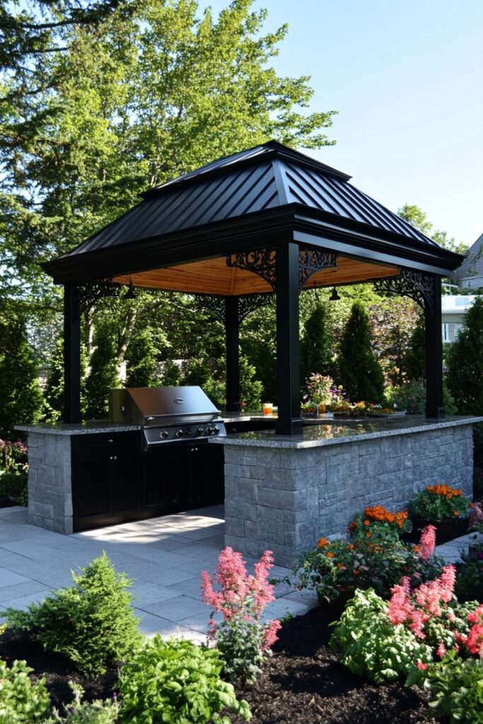 Outdoor grill station under a black metal gazebo with stone base, built-in gas grill, and landscaped backyard garden.