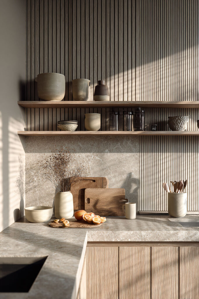 Neutral kitchen with ribbed wood paneling and textured stone backsplash, featuring dimensional surfaces and layered materials in modern organic kitchen design.