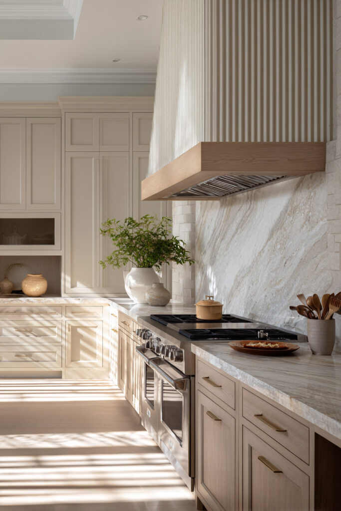 Neutral kitchen with fluted range hood, ribbed paneling, and stone backsplash showcasing dimensional surfaces and textured kitchen design in warm modern style.