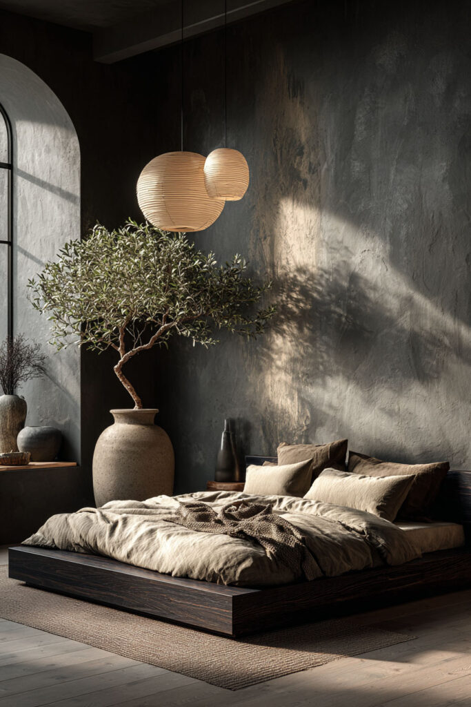 Japandi bedroom with low wood platform bed, dark textured walls, olive tree, and warm neutral bedding with soft natural light