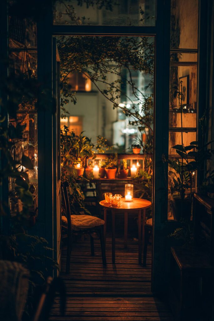 Romantic balcony at night with candlelit bistro table, cozy seating, potted plants, warm lighting, and intimate outdoor dining atmosphere.